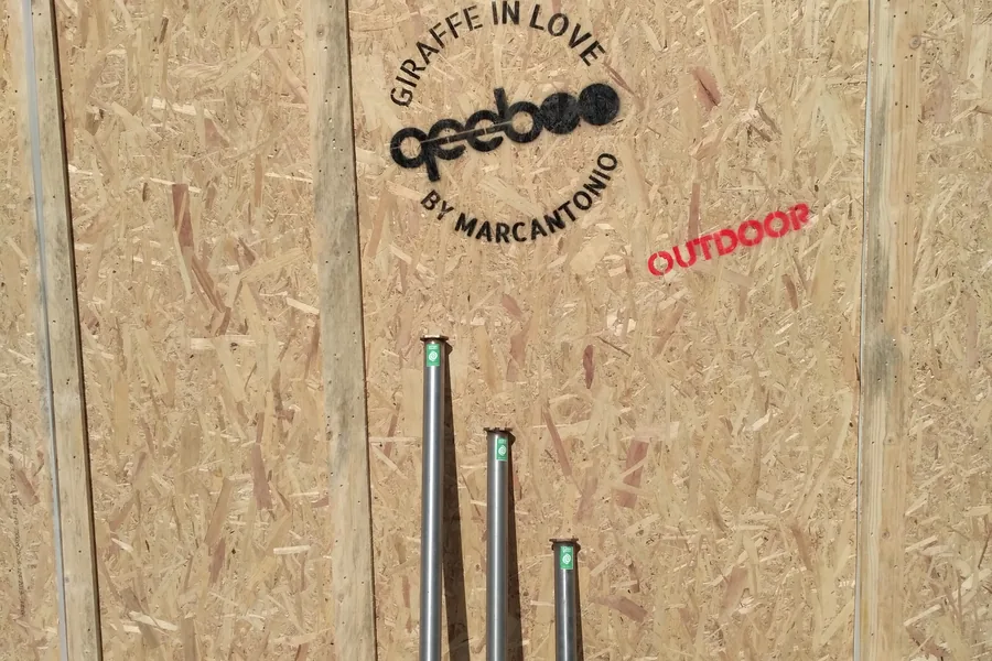 Cassa di legno per il trasporto con il marchio Qeeboo e la scritta «GIRAFFE IN LOVE by Marcantonio — OUTDOOR», con tre fondazioni a vite T-Block appoggiate verticalmente davanti.