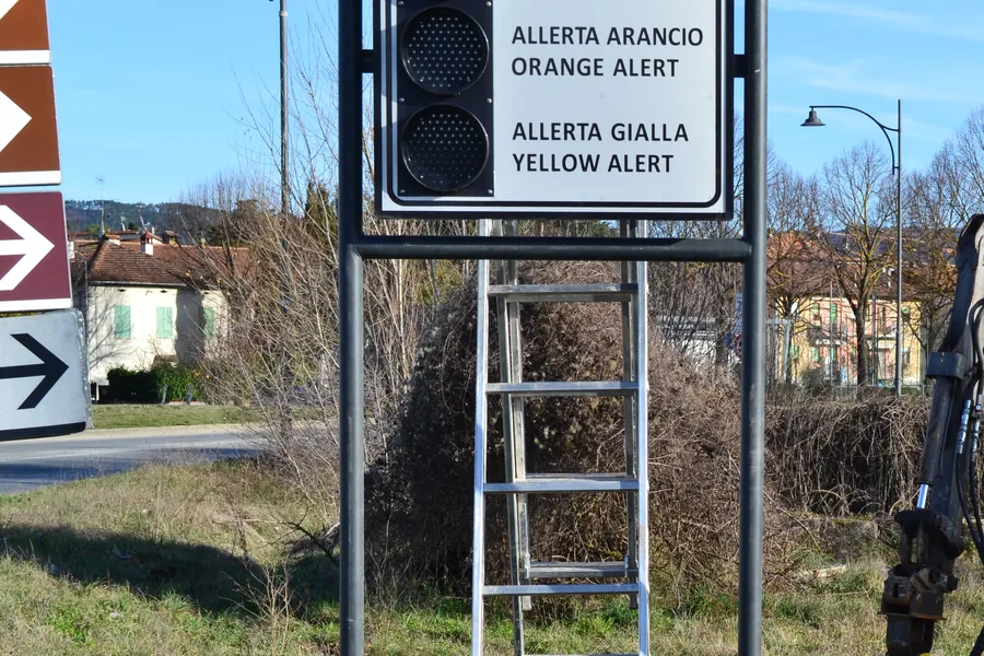 Portale di segnaletica montato a bordo strada con pannelli di allerta e semaforo a due luci, con la testa idraulica di infissione a fianco.