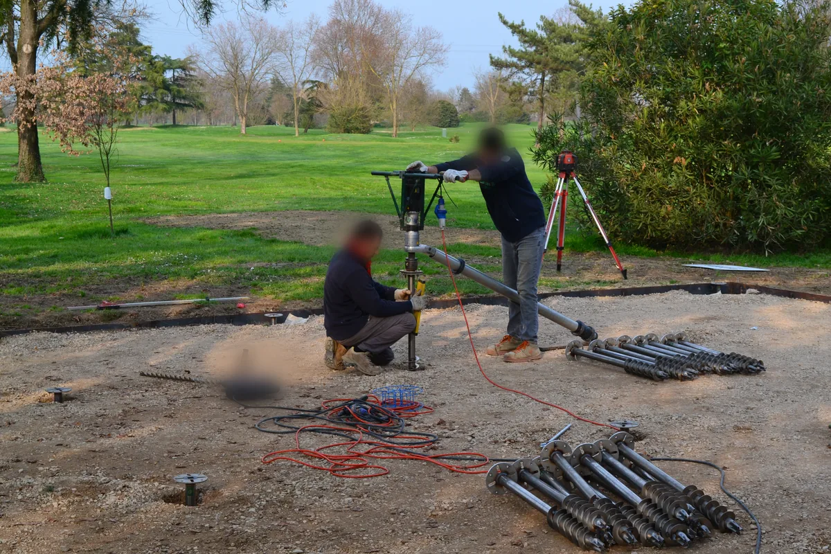 Squadra al lavoro con il TBDriver su un'area in ghiaia, livello laser rotante sul treppiede e T-Block pronti a terra.