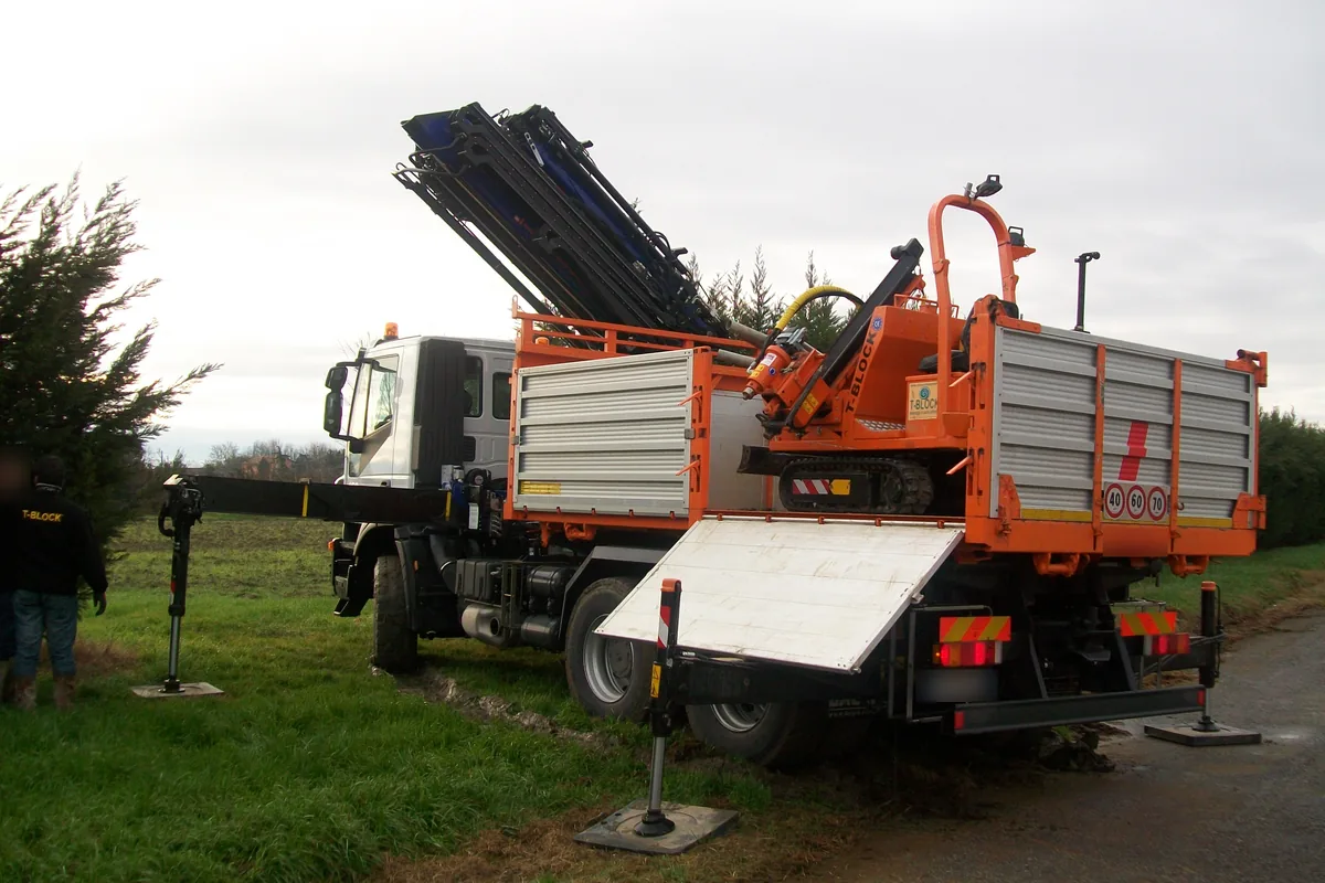 Macchina cingolata arancione con gli adesivi T-Block sul cassone di un camion con gru, con la sponda abbassata come rampa, all'arrivo al campo fotovoltaico di Taglio di Po.