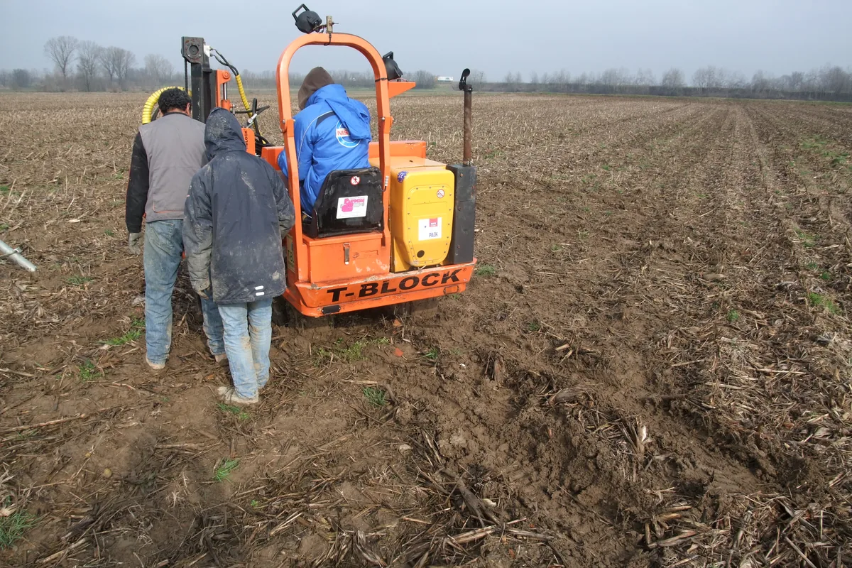 Macchina cingolata arancione T-Block al lavoro in un campo agricolo, con la squadra accanto alla colonna.