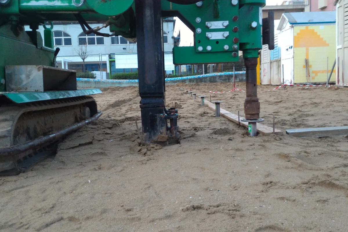 Base della colonna e testa rotativa sopra un T-Block che entra nella sabbia, con le teste già posate sullo sfondo.