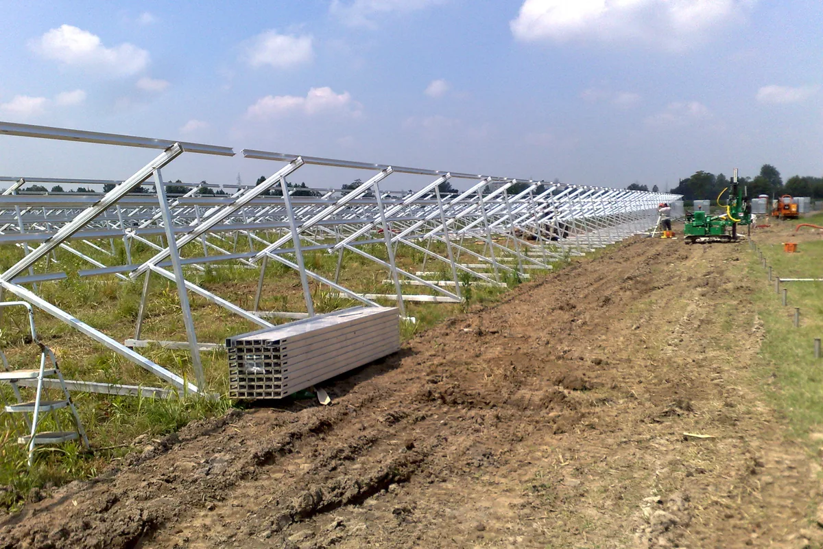 File di strutture in alluminio di un impianto fotovoltaico montate sui T-Block in un campo agricolo.