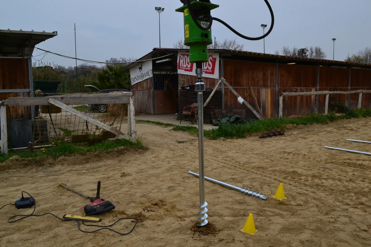 T-Block agganciato alla testa rotativa verde, sollevato in verticale sopra il punto di posa segnato dai coni.