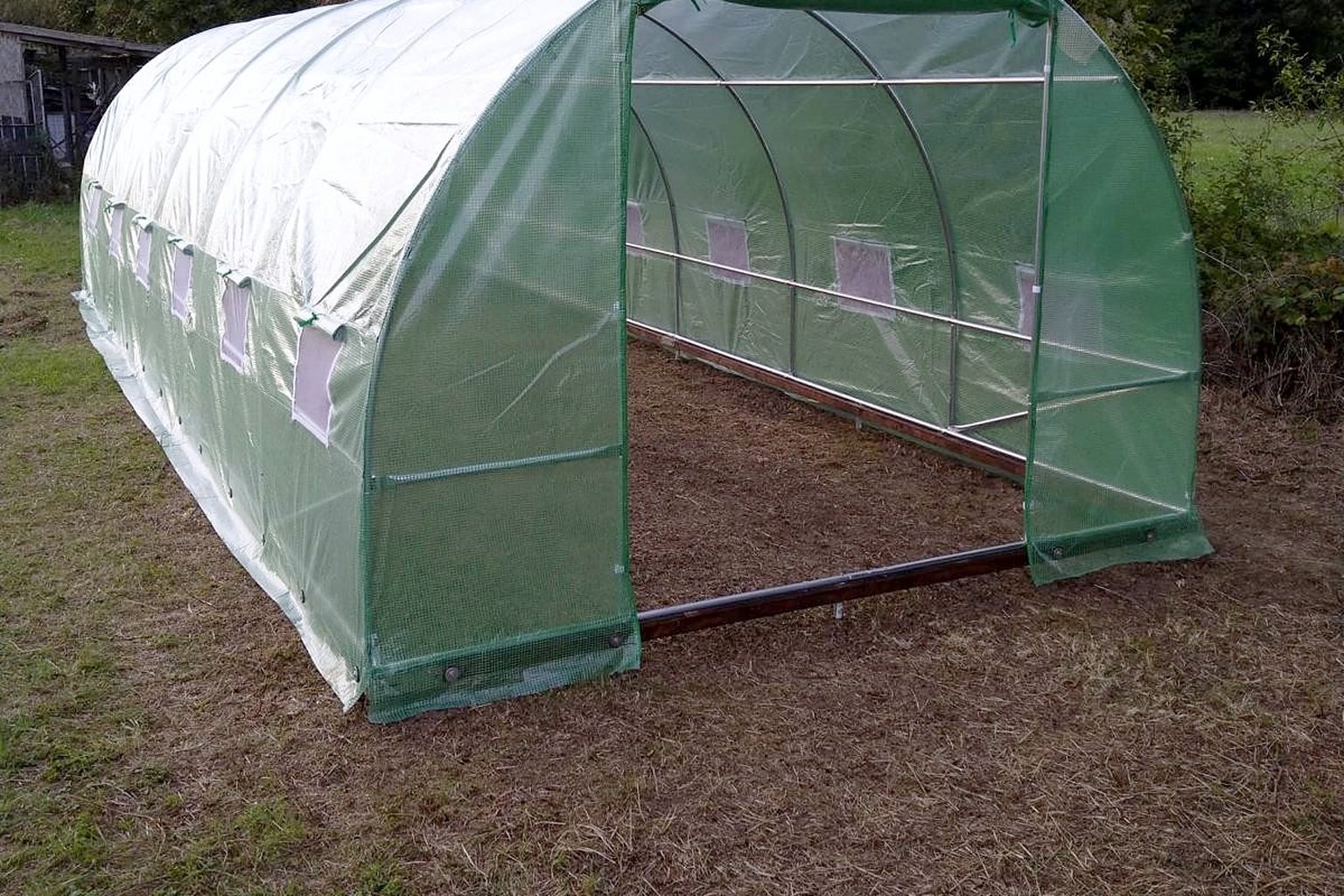 Polytunnel greenhouse with a green sheet fitted on a base frame resting on T-Block ground screws, on a lawn.