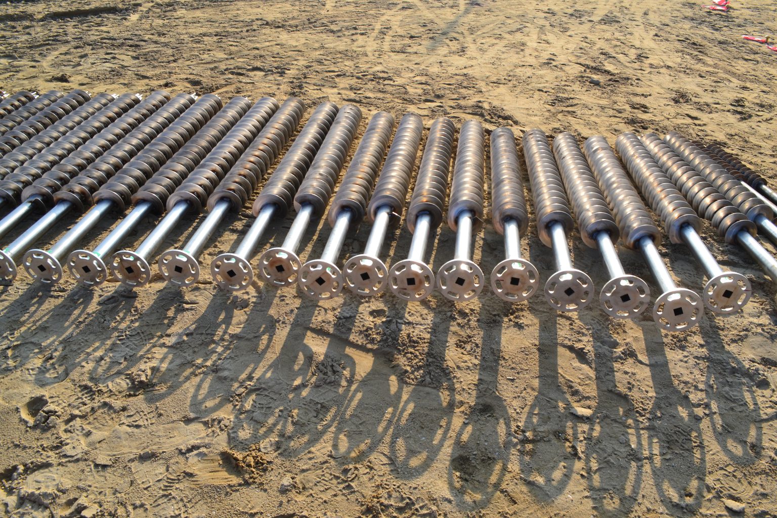 Viti per terreno T-Block in acciaio zincato allineate sulla sabbia di un cantiere, pronte per essere avvitate.