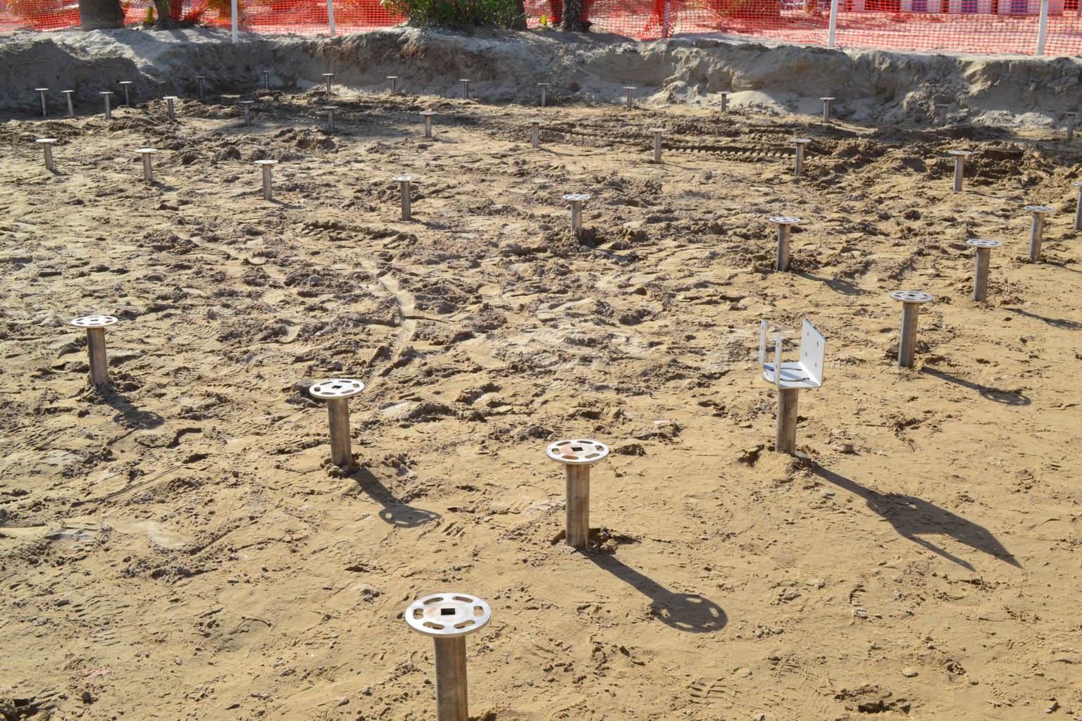 Spiaggia di Giulianova: file di fondazioni a vite T-Block in acciaio inox con la flangia tonda avvitate nella sabbia, una già con la staffa a U.