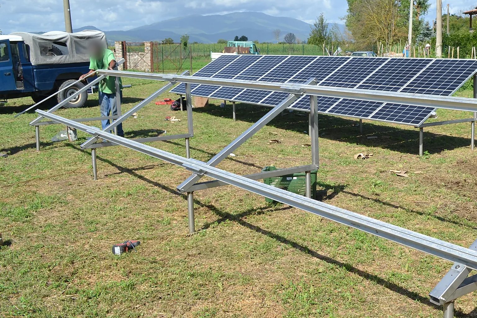 Impianto fotovoltaico a terra in campagna: telai in acciaio inox e alluminio su fondazioni a vite T-Block in acciaio inox con i primi pannelli montati e le colline sullo sfondo.