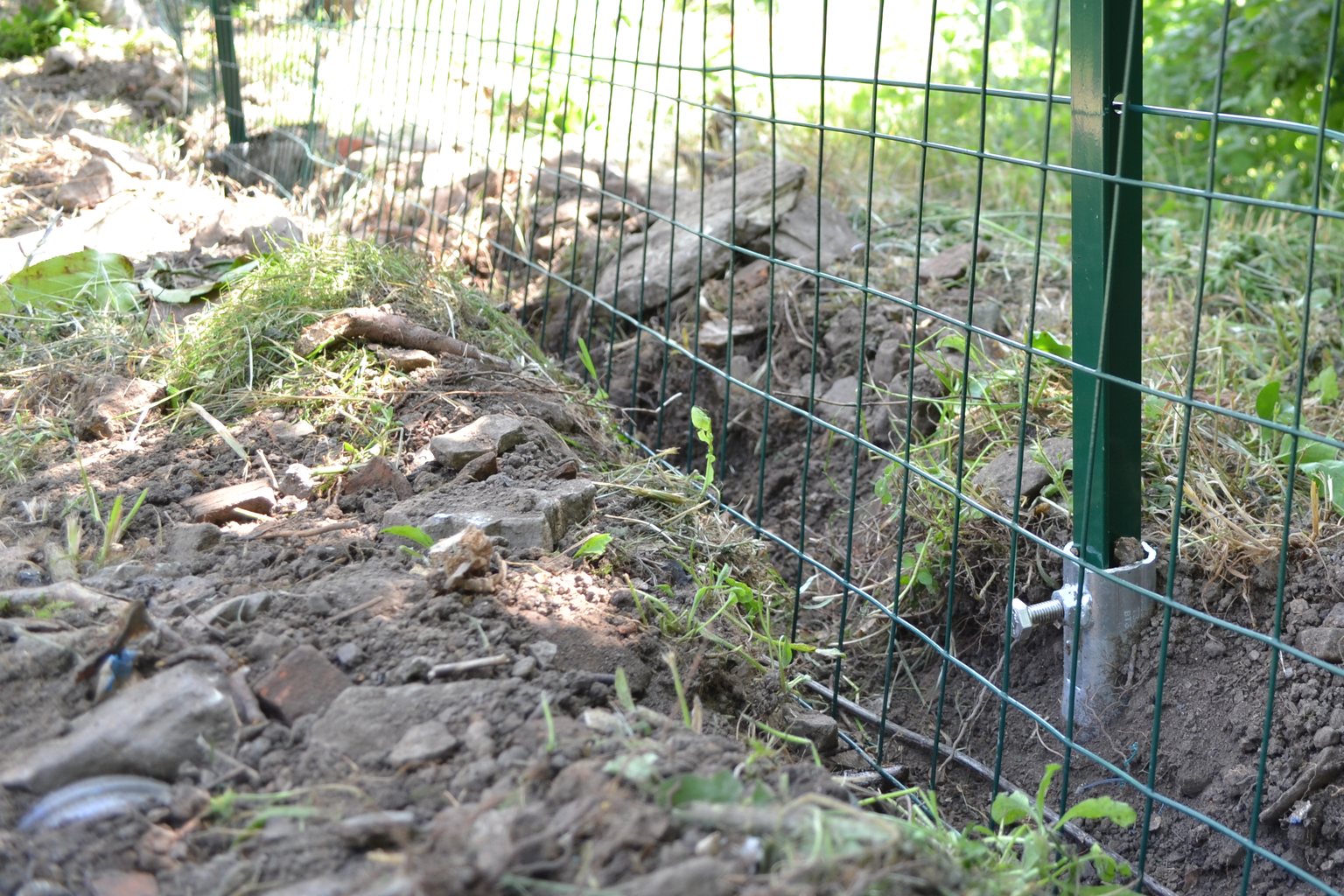 Recinzione a rete verde in un giardino: il palo a T è infilato in una fondazione a vite T-Block avvitata nel terreno, senza plinto.