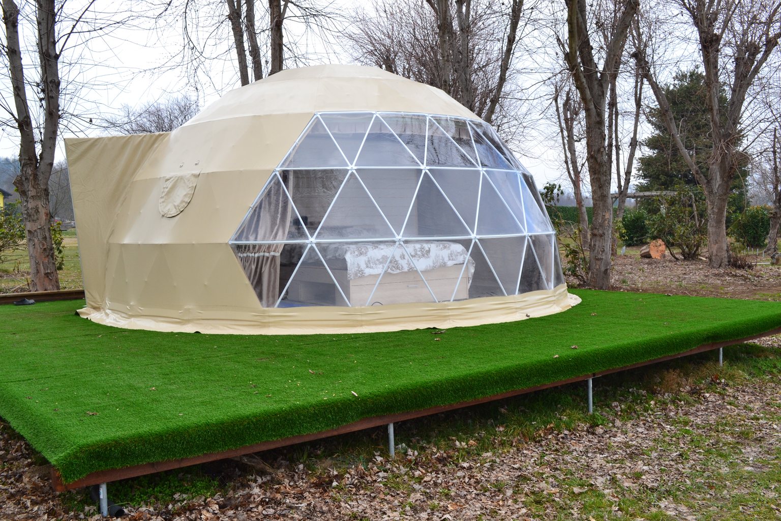 Cupola geodetica per l'ospitalità su una pedana rialzata in un parco, sostenuta da fondazioni a vite T-Block visibili sotto il bordo.