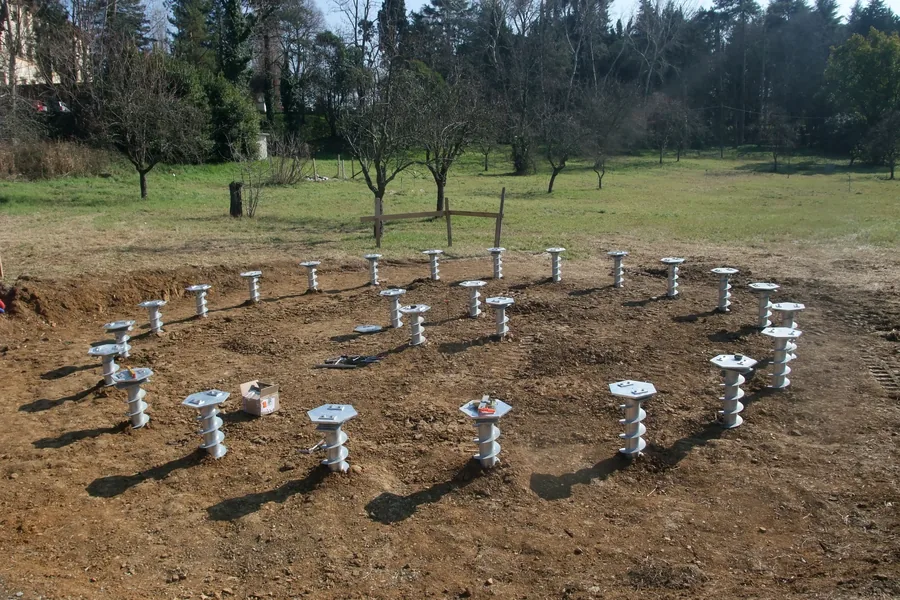 Una trentina di fondazioni a vite T-Block posate in un parco lungo il perimetro della futura cella di prova, con le teste alla stessa quota.