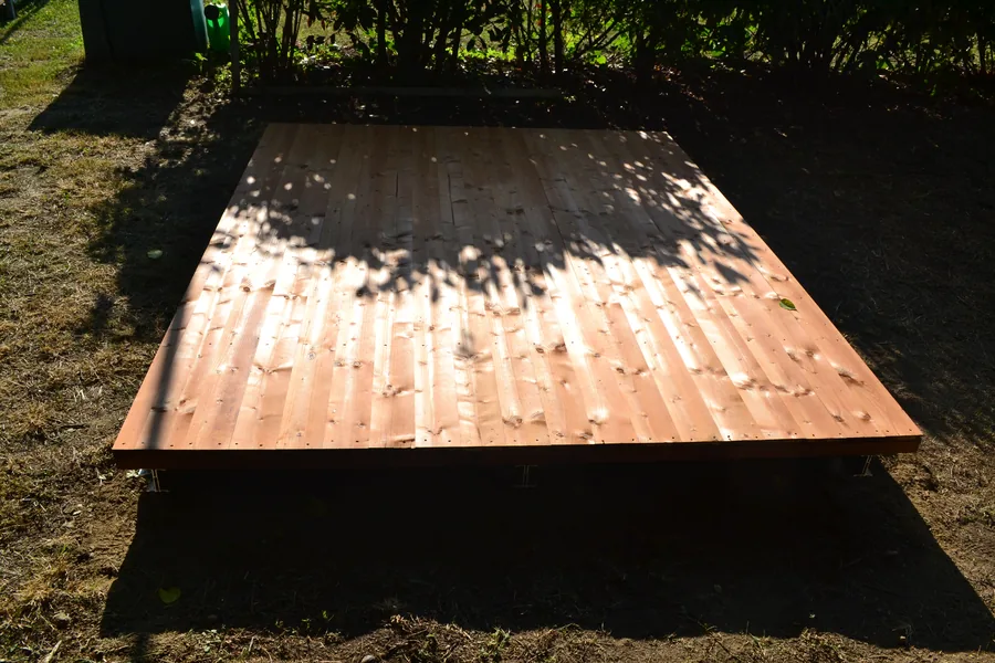 Pedana in legno finita in un giardino, sollevata dal terreno su fondazioni a vite T-Block, senza massetto sotto.