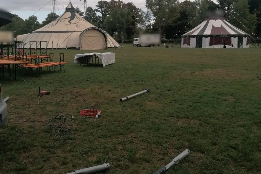 Due grandi tendoni da circo montati sul prato di un parco pubblico, alcune fondazioni a vite T-Block appoggiate sull'erba in primo piano prima della posa.