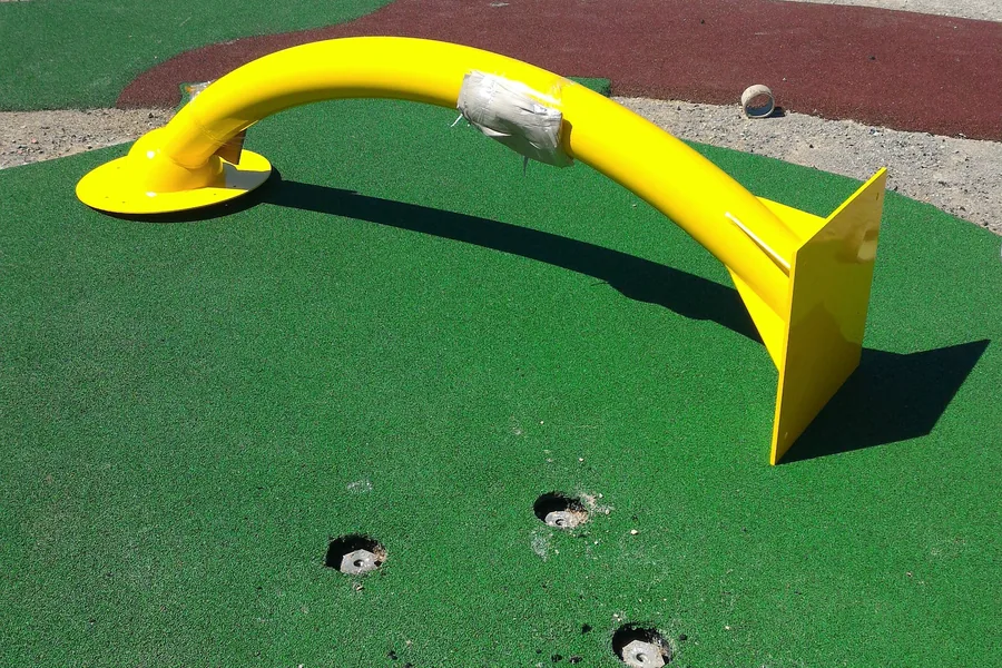 Parco giochi inclusivo: il gioco ad arco sulla pavimentazione antitrauma e, davanti, le teste delle fondazioni a vite T-Block che affiorano dal manto.