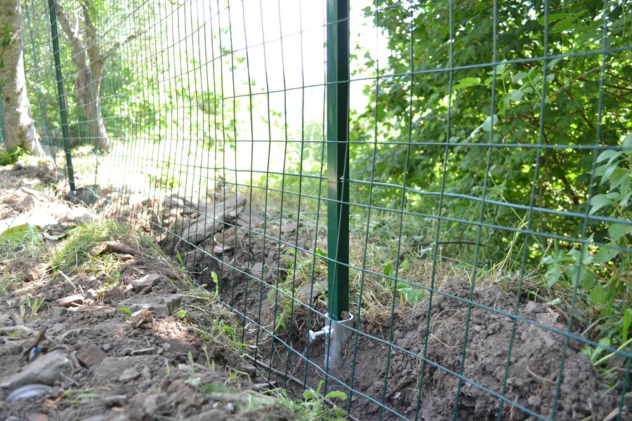 Palo a T verde di una recinzione da giardino avvitato al terreno con una fondazione a vite T-Block specifica, con la rete metallica gia' montata: nessun plinto di calcestruzzo alla base.