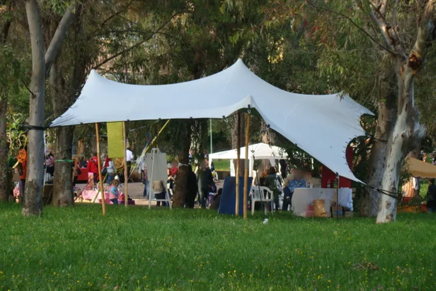 Tensostruttura fra gli alberi di un parco durante un evento, con i T-Block per il fissaggio su prato erboso.