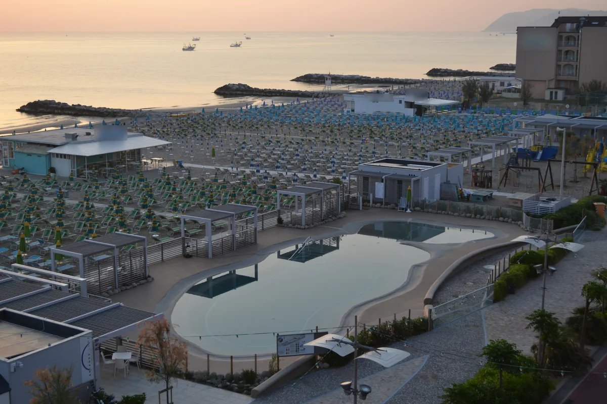 Lo stabilimento Spiagge Luna visto dall'alto all'alba: la piscina, le pergole bianche, gli ombrelloni chiusi e il mare calmo con le scogliere.