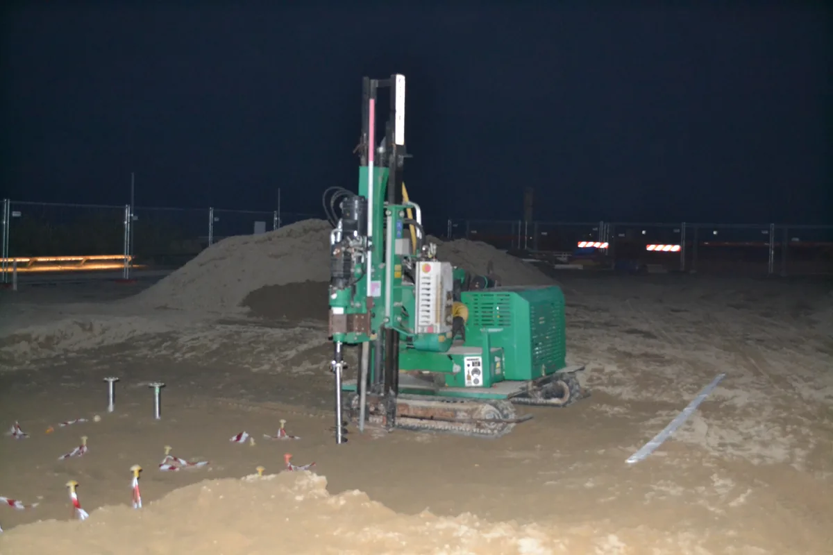 La macchina cingolata a colonna al lavoro sulla spiaggia di notte, con i picchetti segnati sulla sabbia e le prime teste già posate.
