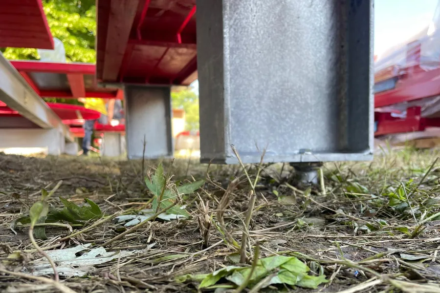 Seduta di arredo urbano sul prato, vista da terra: il piede della panchina appoggia sulla testa di una ancoraggio a vite T-Block inserito nel terreno.