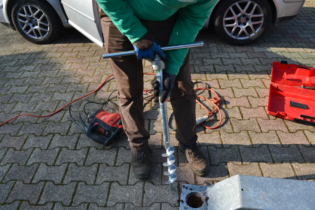 Operatore che avvita una fondazione a vite T-Block attraverso la pavimentazione in masselli autobloccanti di un cortile, usando un avvitatore a mano.