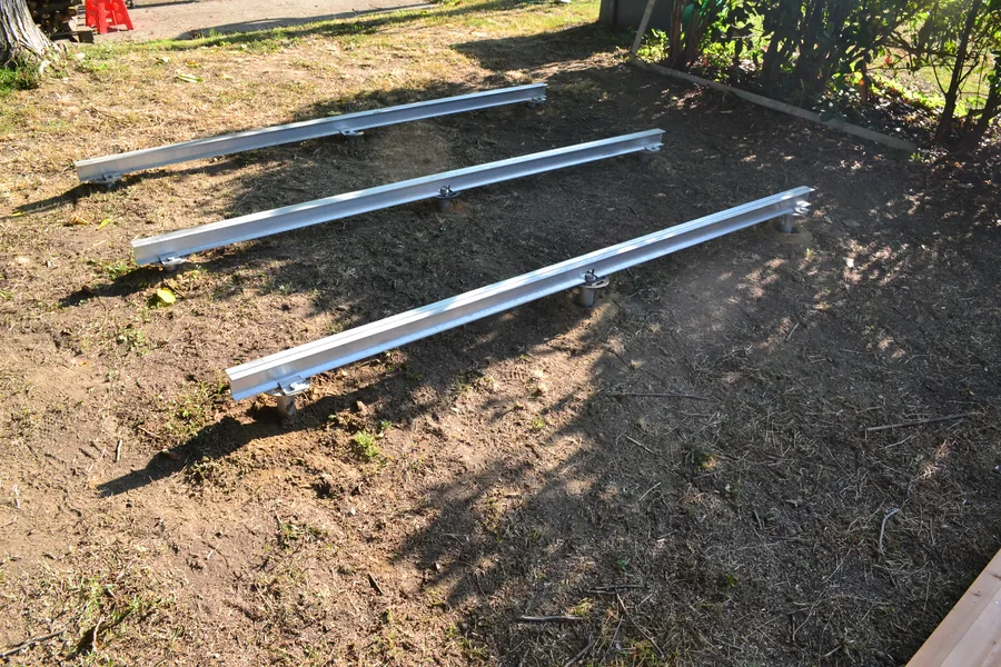 Tre profili metallici paralleli fissati sulle fondazioni a vite T-Block in un giardino: il telaio della casetta prima del pavimento.