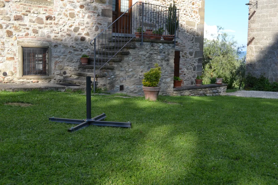 La base a croce e l'asta dell'ombrellone montate sulle teste degli ancoraggi a vite T-Block, sul prato davanti al casale.