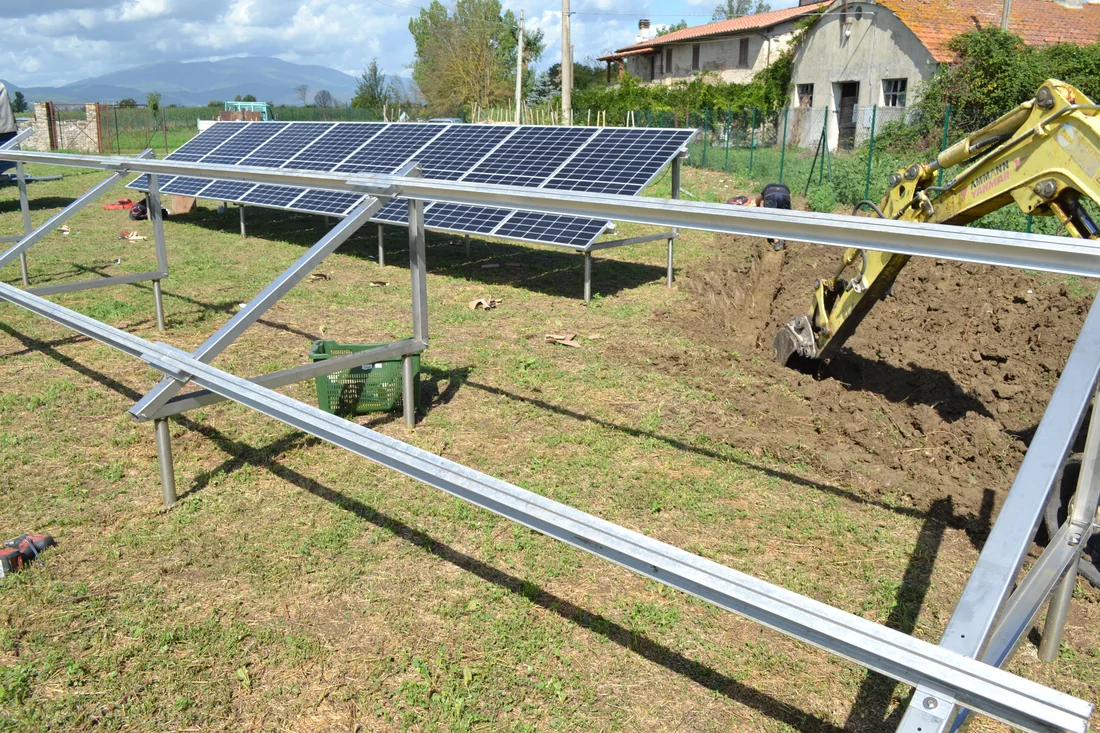 File di moduli fotovoltaici montati sulla struttura in acciaio ancorata con fondazioni a vite T-Block, in un terreno agricolo.