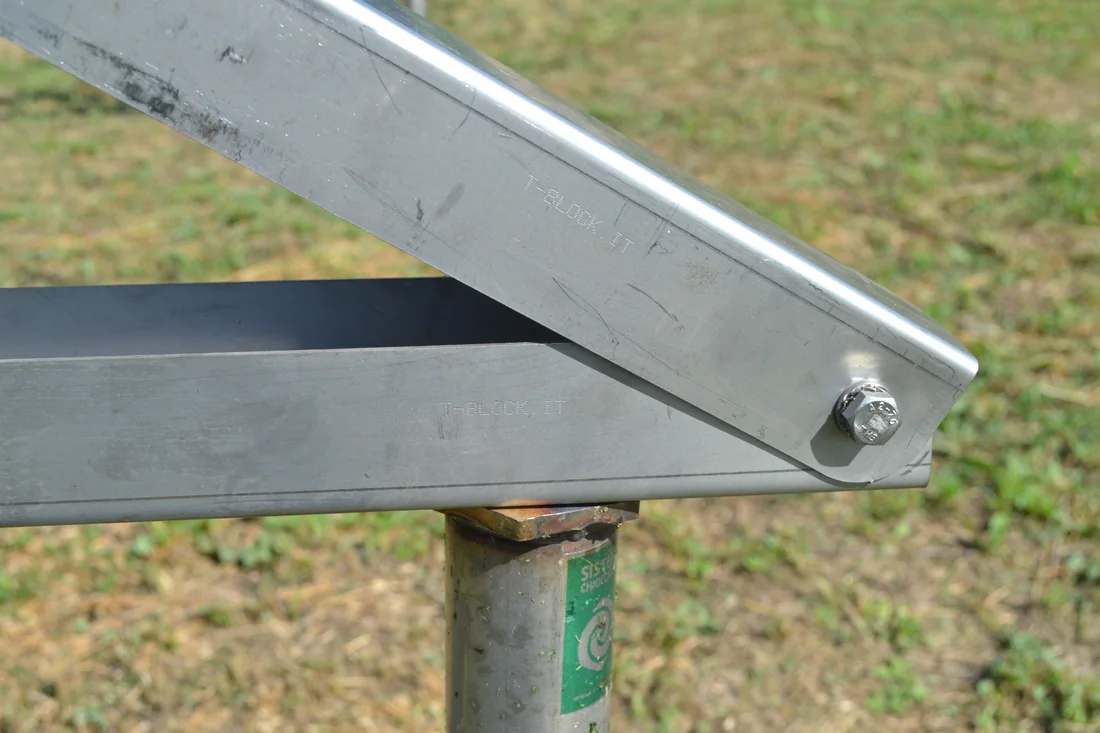 Dettaglio della testa a flangia di una fondazione a vite T-Block che sostiene la trave inclinata della struttura fotovoltaica, con il prato intorno intatto.