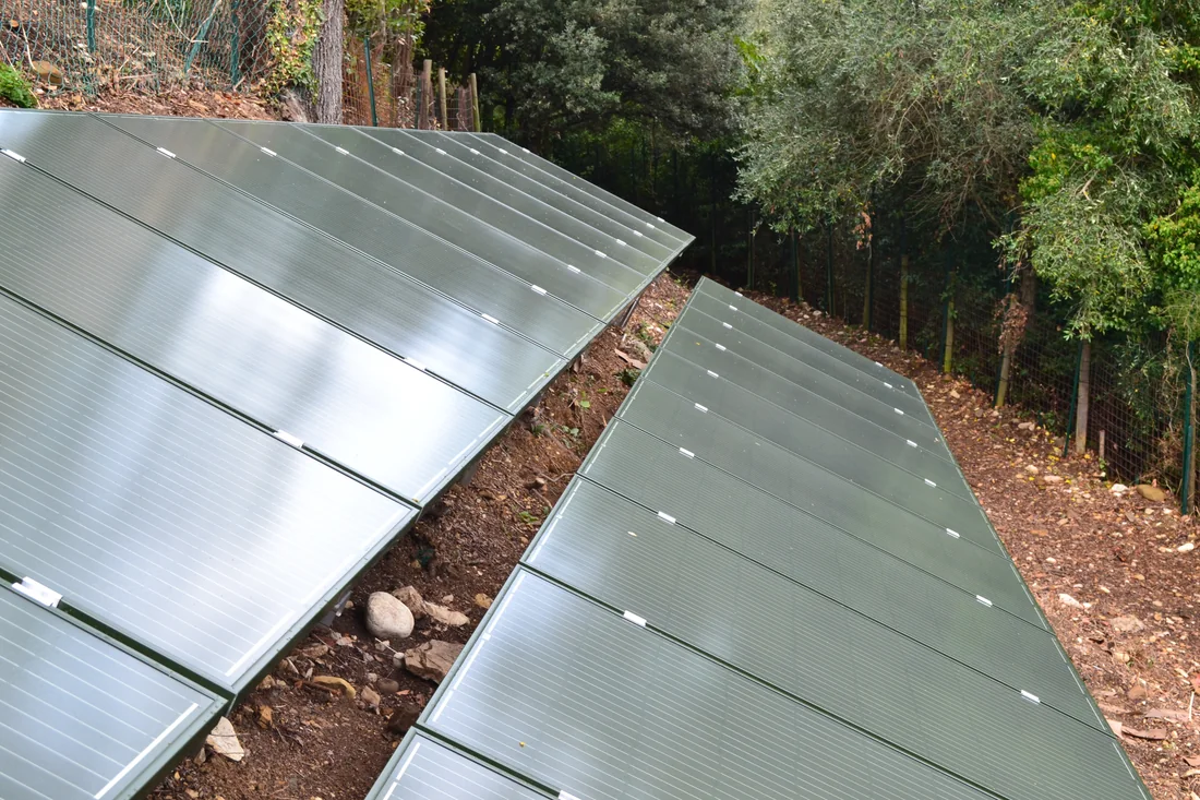 Impianto fotovoltaico a terra su terreno in pendenza: file di pannelli su guide metalliche sostenute da fondazioni a vite T-Block.