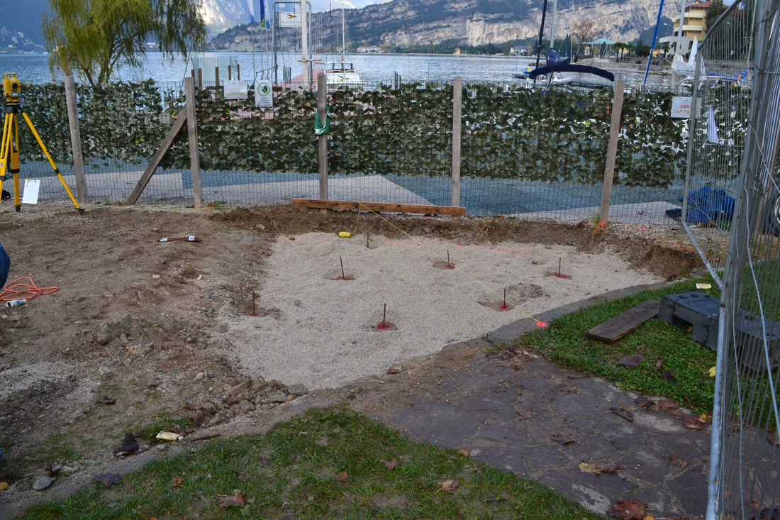 Area di installazione con le fondazioni a vite T-Block già posate secondo lo schema di ancoraggio, sul fronte lago di Torbole con le montagne sullo sfondo.