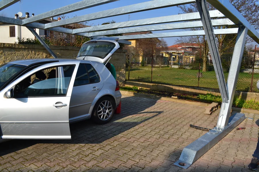 Carport in acciaio su un giardino privato pavimentato con autobloccanti: il piede della struttura appoggia direttamente sulla pavimentazione, senza plinto ed è fissato al suolo tramite viti T-Block.