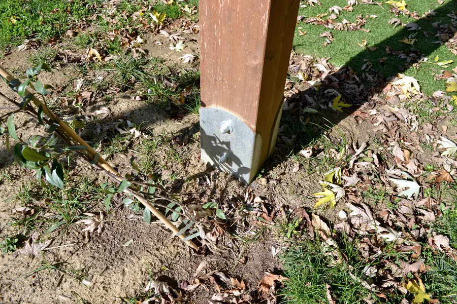 Pied d’un poteau en bois de la pergola dans un sabot en acier galvanisé au ras de la pelouse, au-dessus de la vis de fondation T-Block.