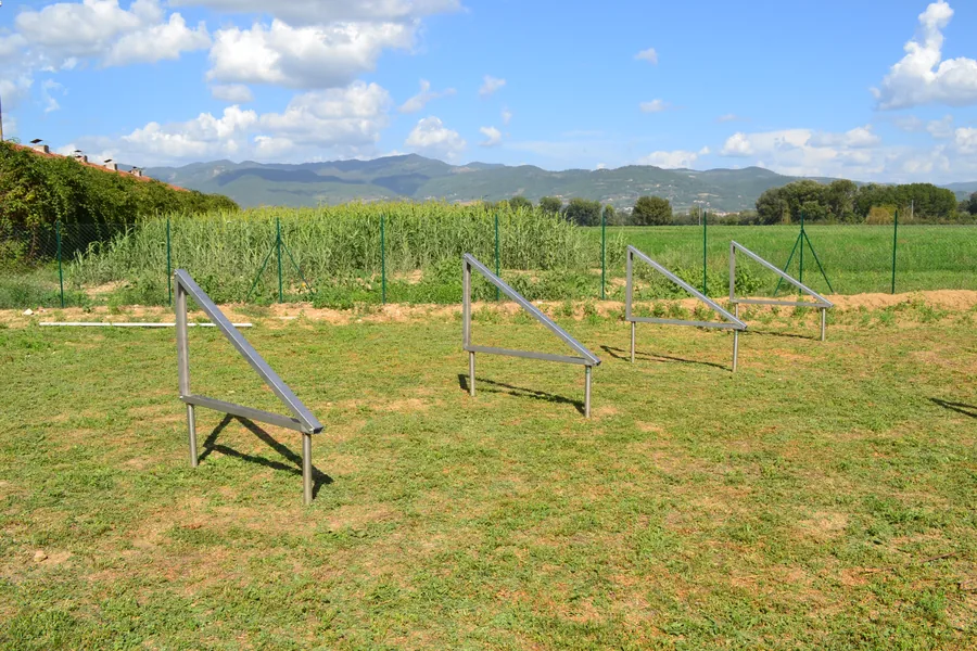 Strutture fotovoltaiche in acciaio montate su fondazioni a vite T-Block in un campo di campagna, con le colline sullo sfondo.