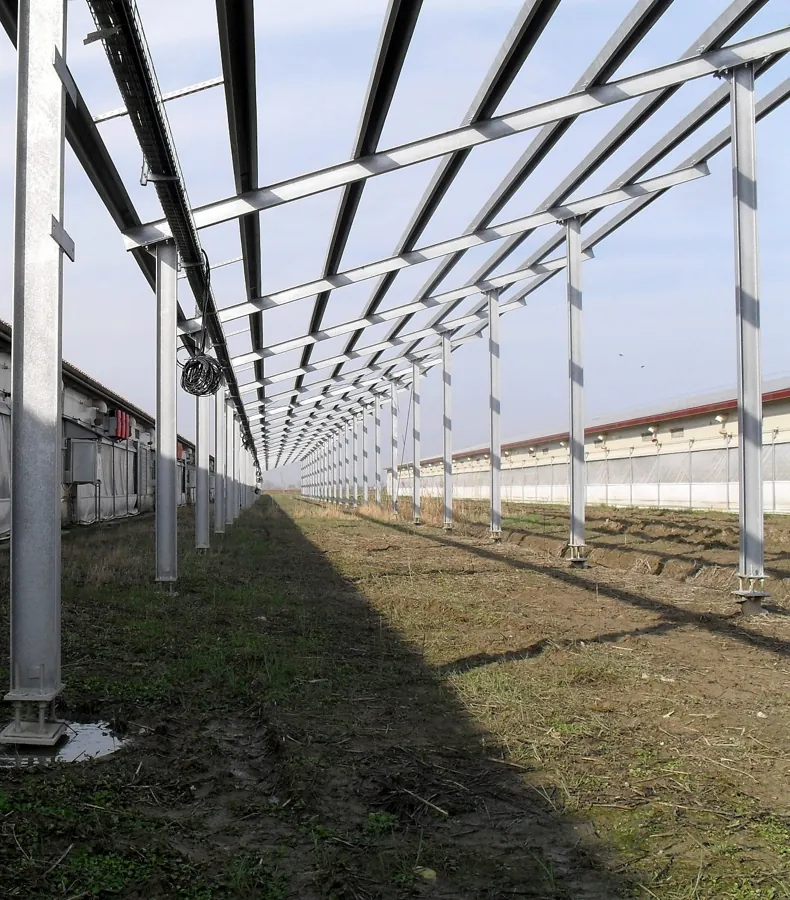 Lunga struttura in acciaio zincato su colonne fra due capannoni agricoli: ogni colonna poggia su una fondazione a vite T-Block flangiata.