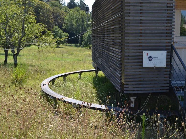 La test cell completata in un prato: rivestimento in listelli di legno, struttura sollevata dal terreno sulle fondazioni a vite T-Block.