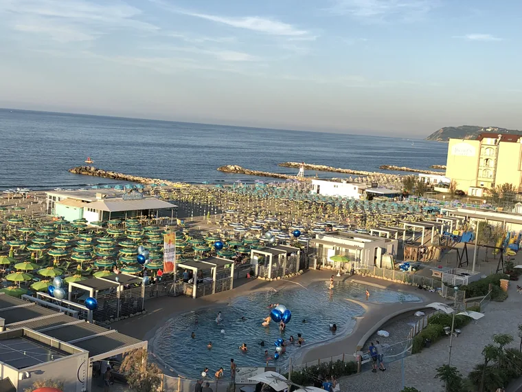 Stabilimento balneare con piscina e file di ombrelloni sulla spiaggia, realizzato su fondazioni a vite T-Block in acciaio inox.
