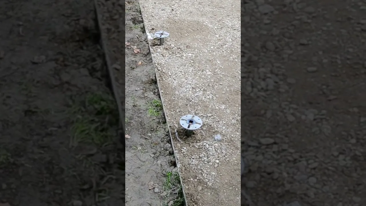 Le teste a flangia di due T-Block già avvitati in una striscia di ghiaia, accanto al terreno.