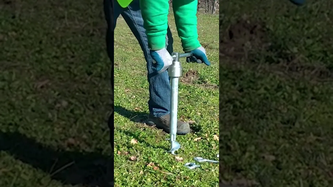Un opérateur en pull vert, penché sur la pelouse, visse à la main un ancrage T-Block avec la clé en T.