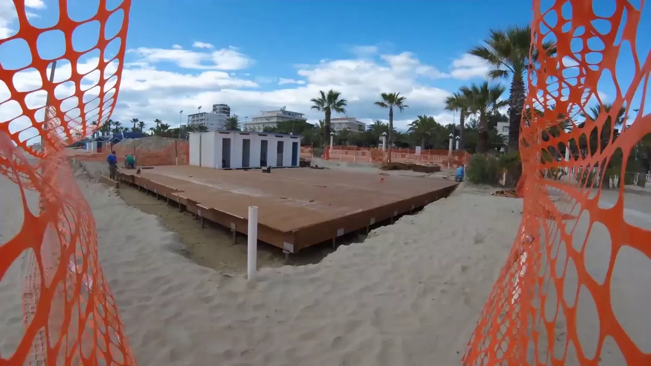 La pedana in legno in costruzione sulla spiaggia di Giulianova, fra le reti arancioni del cantiere e le palme.