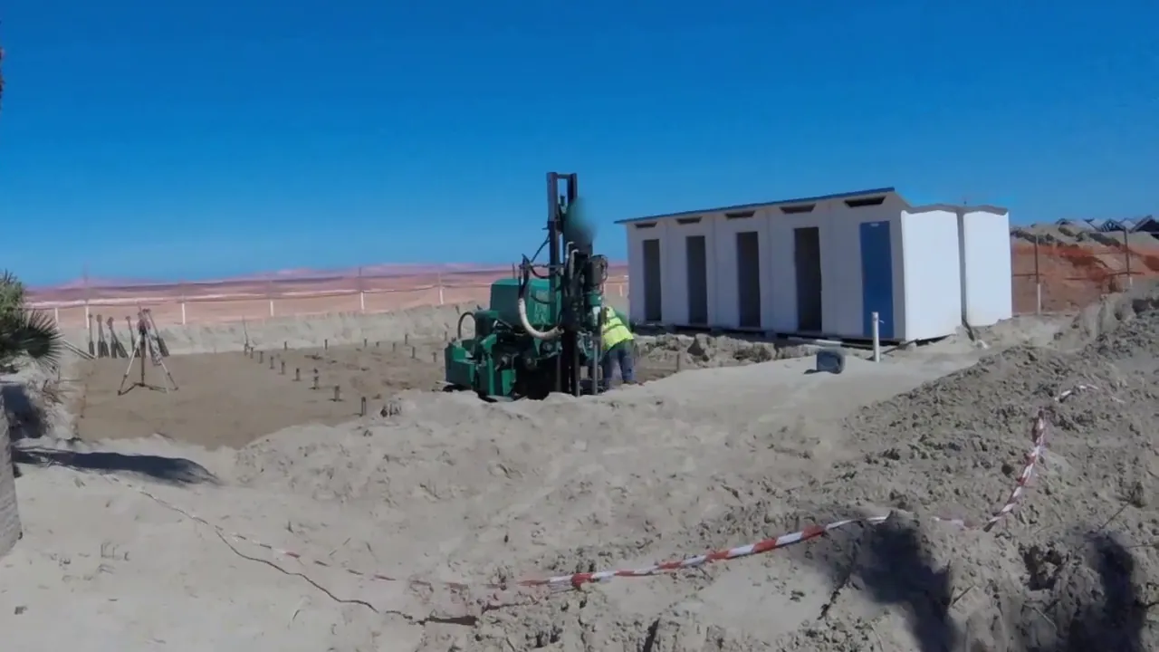 La macchina cingolata a colonna sulla spiaggia di Giulianova, accanto alle cabine bianche, sotto il cielo azzurro.