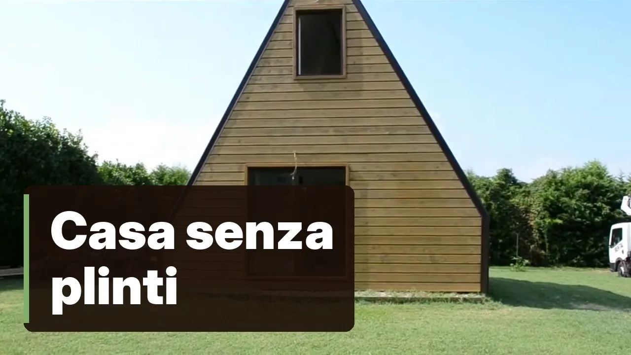 Una casa in legno a forma di capanna triangolare sul prato, con la scritta «Casa senza plinti».