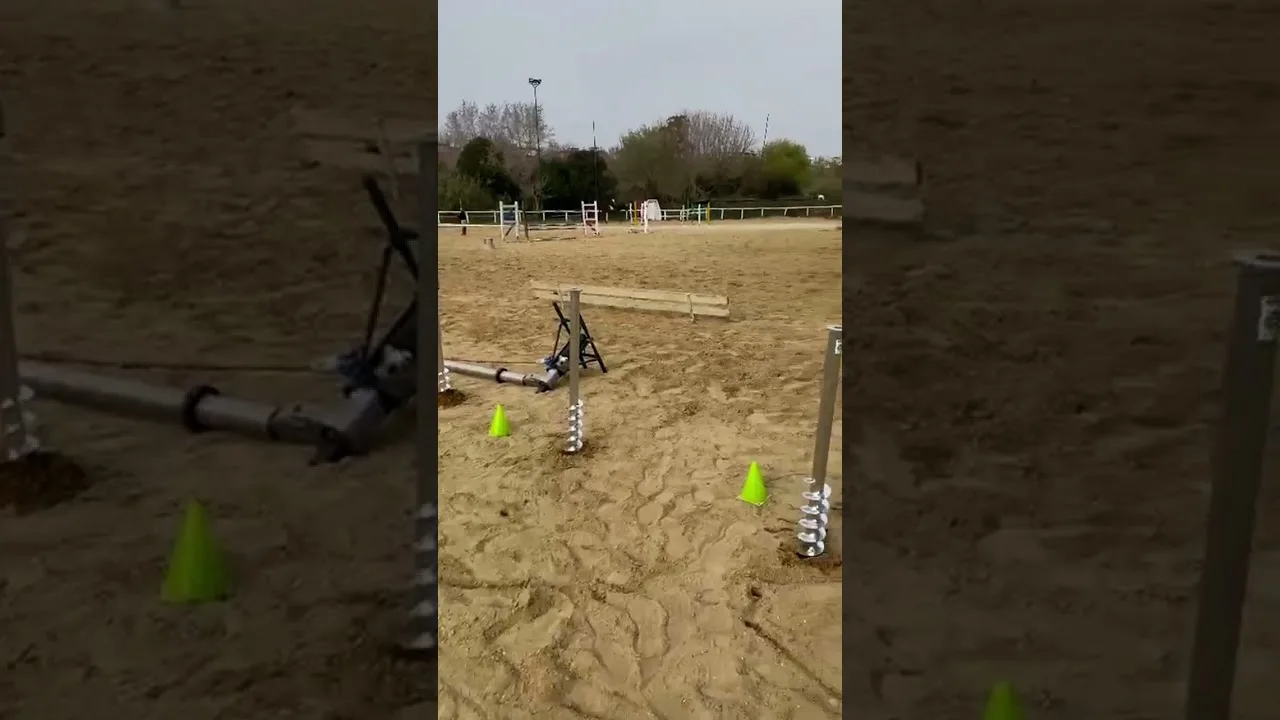 Un campo da equitazione in sabbia con ostacoli e coni verdi, e una vite T-Block piantata a bordo.