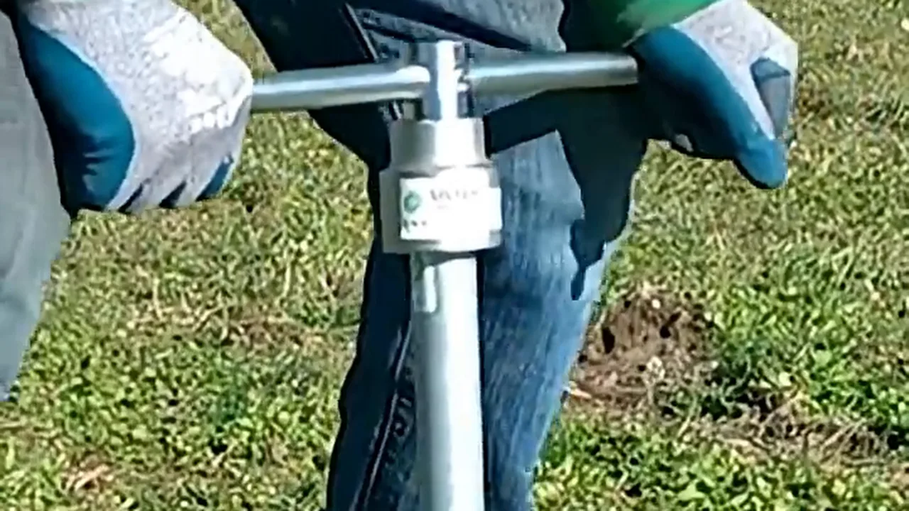 Mani con i guanti che girano il manico a T sulla testa di un T-Block nel prato.